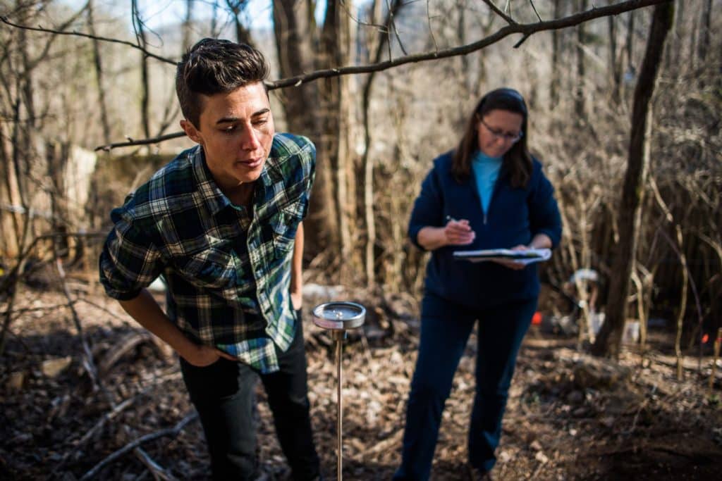 person standing with thermometer of human composting pile