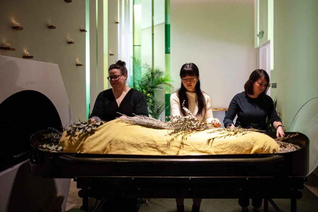 People standing by shrouded mannequin at a funeral service