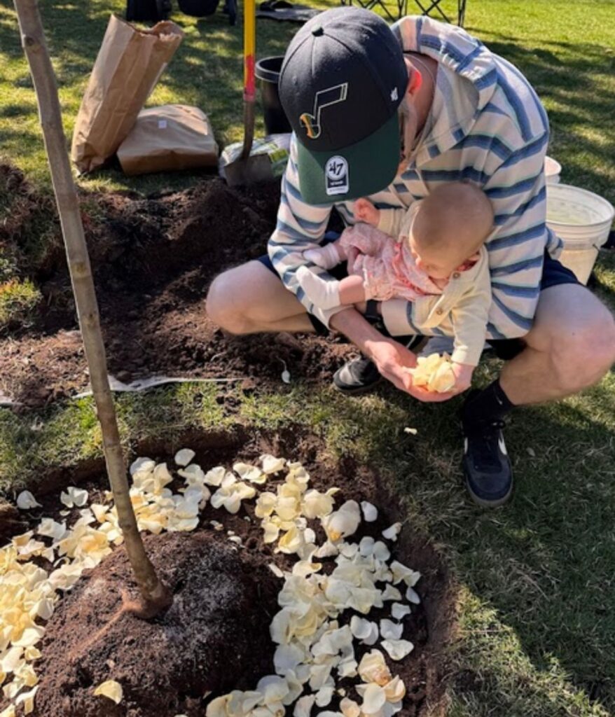 man holding baby by a tree with flowers around the base of the tree